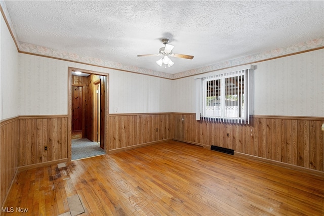 empty room featuring wood-type flooring, a textured ceiling, wooden walls, and ceiling fan