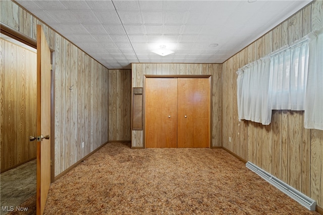 unfurnished bedroom featuring carpet floors, wooden walls, a closet, and a baseboard radiator