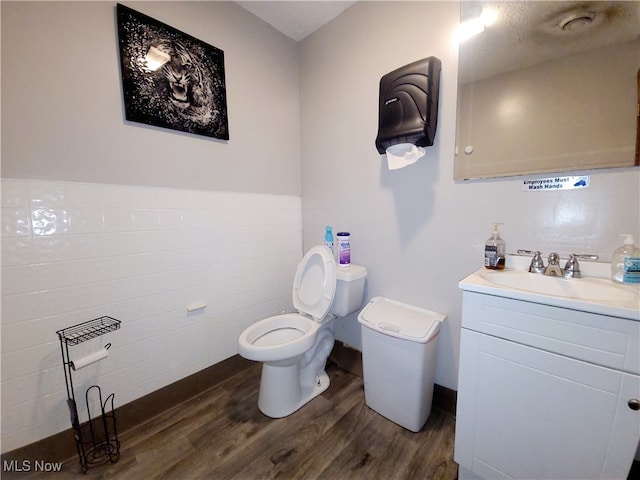 bathroom with tile walls, hardwood / wood-style floors, vanity, and toilet