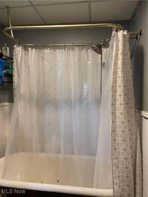 bathroom with a drop ceiling and shower / bathtub combination with curtain