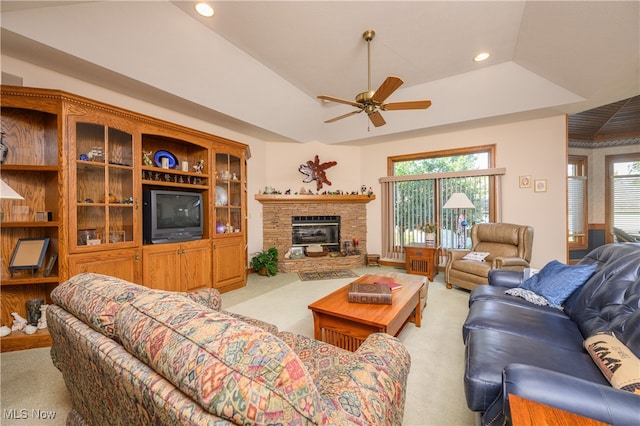 carpeted living room featuring ceiling fan, a raised ceiling, plenty of natural light, and a stone fireplace