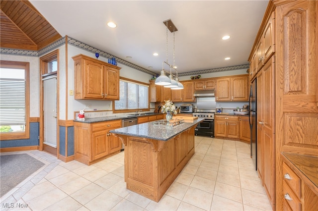 kitchen featuring dark stone counters, stainless steel appliances, a center island, and a healthy amount of sunlight