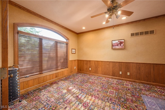 empty room with ornamental molding, wood walls, and ceiling fan