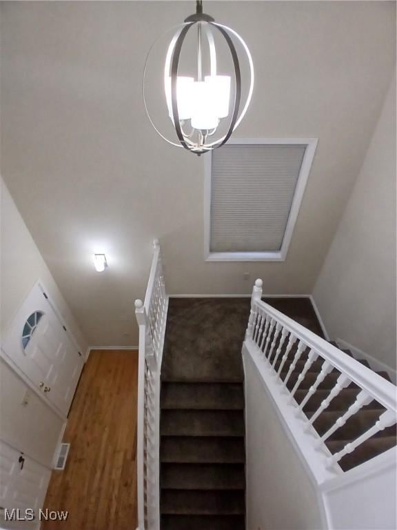 stairs with hardwood / wood-style floors and an inviting chandelier