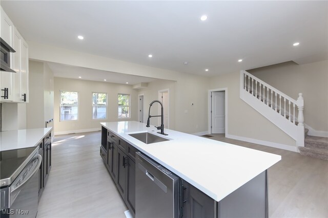 kitchen with light wood-type flooring, sink, white cabinetry, stainless steel appliances, and a center island with sink