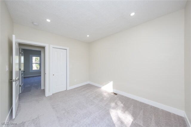 unfurnished bedroom with light carpet, a textured ceiling, and a closet