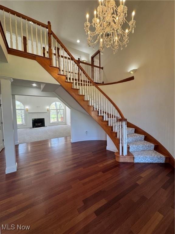 unfurnished living room with a towering ceiling, wood finished floors, baseboards, an inviting chandelier, and stairs