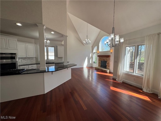kitchen featuring dark countertops, a notable chandelier, double oven, open floor plan, and dark wood-style floors