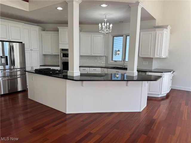 kitchen with backsplash, stainless steel appliances, dark countertops, and ornate columns