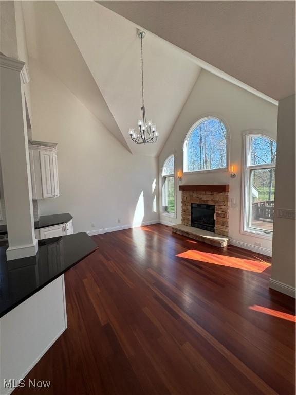 unfurnished living room with high vaulted ceiling, plenty of natural light, a stone fireplace, and dark wood-type flooring