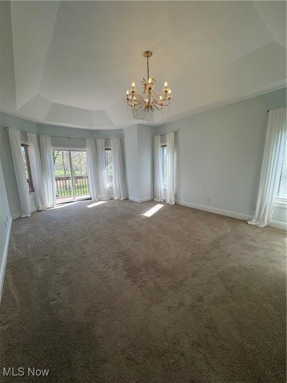carpeted empty room featuring a raised ceiling, baseboards, and a chandelier