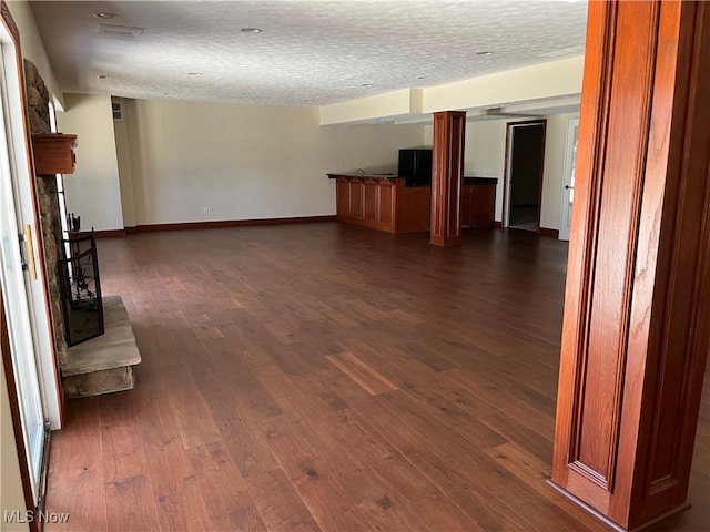 unfurnished living room featuring dark wood-style flooring, a textured ceiling, and baseboards