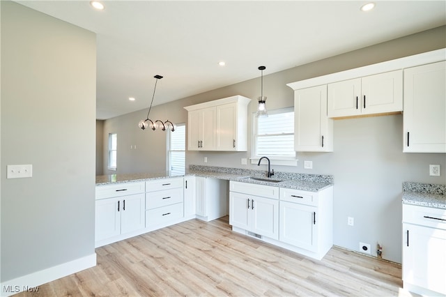 kitchen featuring pendant lighting, sink, light wood-type flooring, and white cabinetry