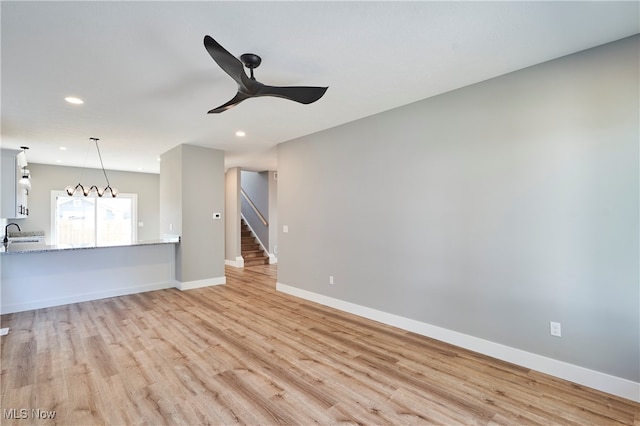 unfurnished living room featuring ceiling fan with notable chandelier, sink, and light hardwood / wood-style floors