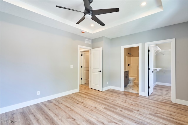 unfurnished bedroom featuring ceiling fan, light wood-type flooring, ensuite bathroom, and a spacious closet