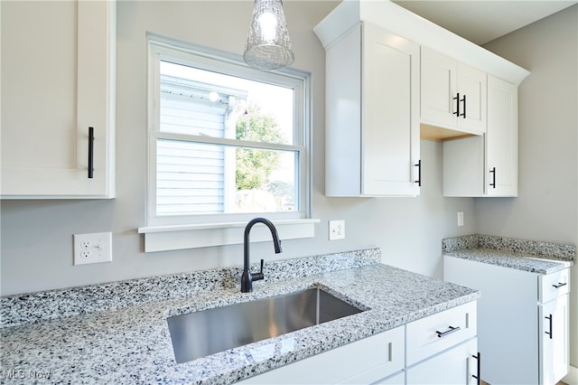 kitchen with light stone countertops, decorative light fixtures, sink, and white cabinetry