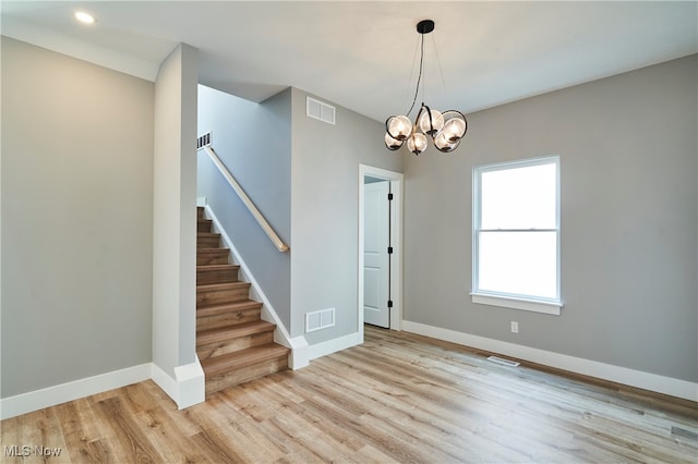 empty room with a notable chandelier and light hardwood / wood-style floors