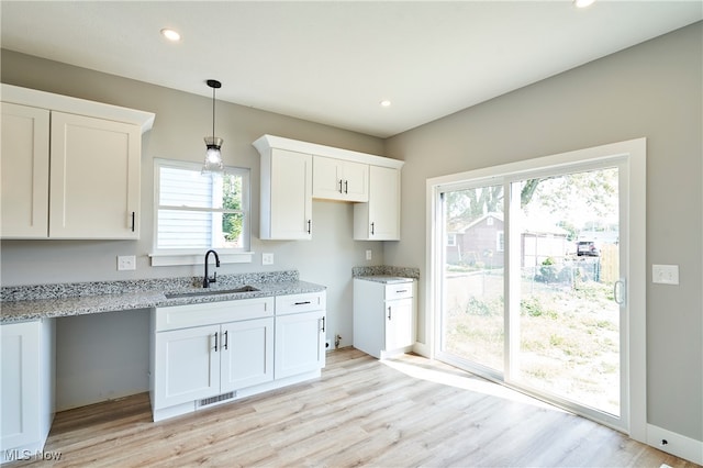 kitchen featuring light stone counters, pendant lighting, sink, light hardwood / wood-style flooring, and white cabinetry