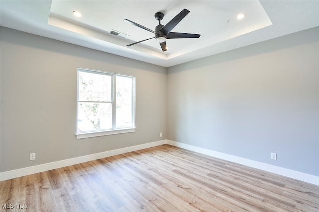 unfurnished room with ceiling fan, a tray ceiling, and light hardwood / wood-style flooring