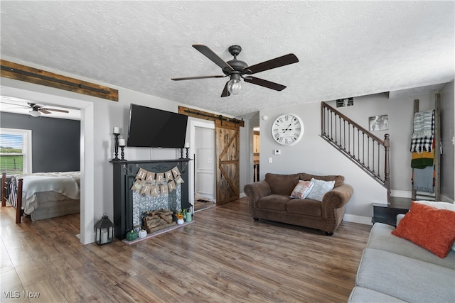 living room featuring a barn door, a textured ceiling, dark hardwood / wood-style floors, and ceiling fan