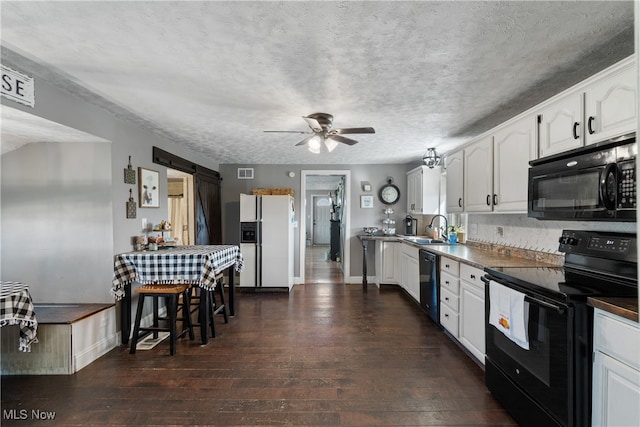 kitchen with white cabinets, black appliances, dark hardwood / wood-style floors, and a barn door