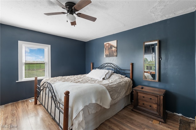 bedroom with ceiling fan, multiple windows, hardwood / wood-style floors, and a textured ceiling