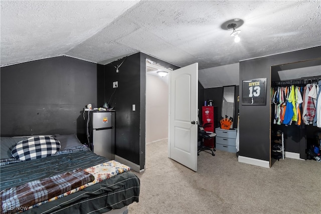 carpeted bedroom with a textured ceiling, stainless steel fridge, and vaulted ceiling