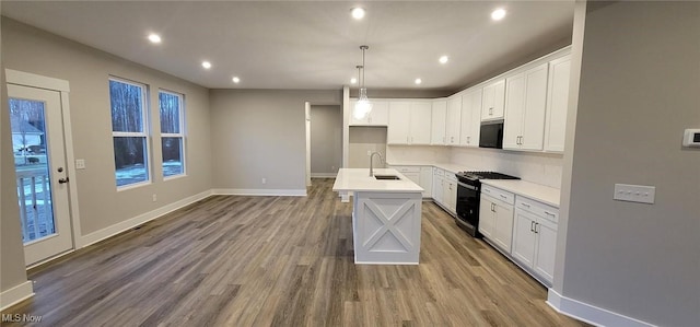 kitchen with sink, white cabinetry, hanging light fixtures, range with gas stovetop, and a center island with sink