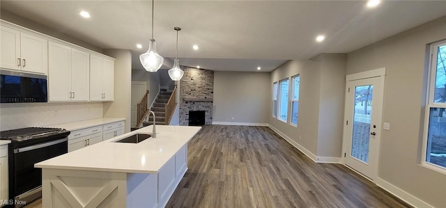 kitchen with stainless steel gas stove, sink, an island with sink, and white cabinets