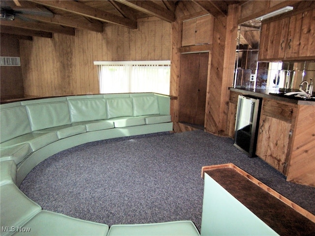 carpeted living room with bar area, wood walls, and beam ceiling