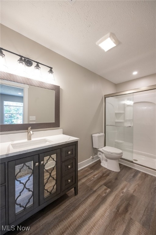 bathroom featuring a textured ceiling, a shower with door, hardwood / wood-style floors, vanity, and toilet