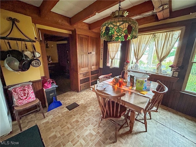 dining area featuring beamed ceiling and wood walls