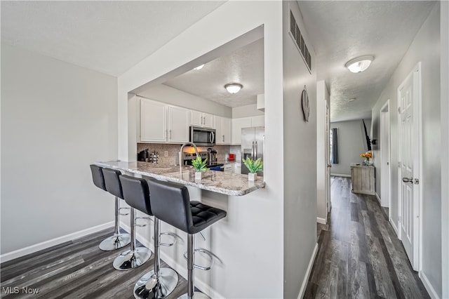 kitchen with white cabinets, kitchen peninsula, a textured ceiling, appliances with stainless steel finishes, and a kitchen breakfast bar