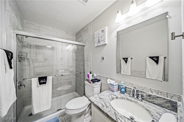 bathroom with a textured ceiling, a shower with shower door, vanity, and toilet