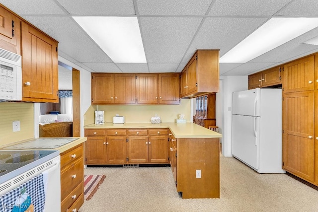 kitchen with kitchen peninsula, white appliances, light colored carpet, and a drop ceiling