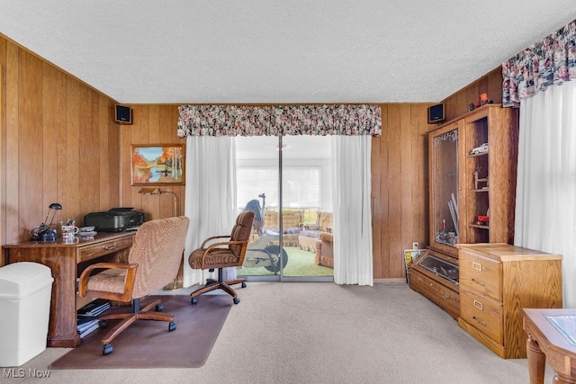 carpeted home office with a textured ceiling and wooden walls