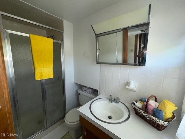 bathroom with walk in shower, vanity, toilet, and tile walls