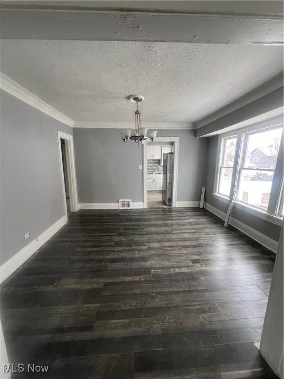 interior space with dark wood-type flooring, a textured ceiling, ornamental molding, and a notable chandelier