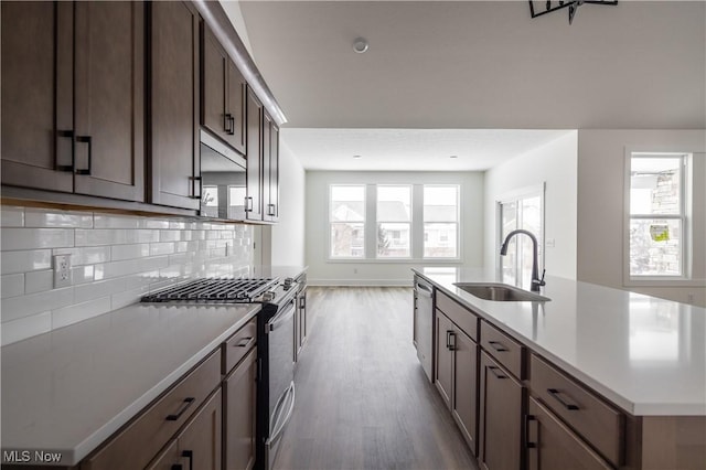 kitchen with sink, decorative backsplash, hardwood / wood-style flooring, a kitchen island with sink, and stainless steel appliances