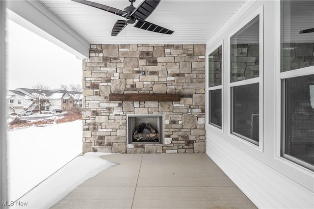 snow covered patio featuring ceiling fan and an outdoor stone fireplace