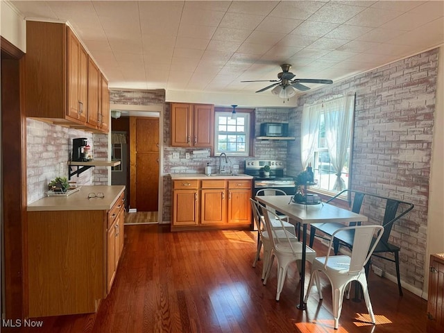 kitchen with dark hardwood / wood-style flooring, brick wall, stainless steel electric stove, ceiling fan, and sink