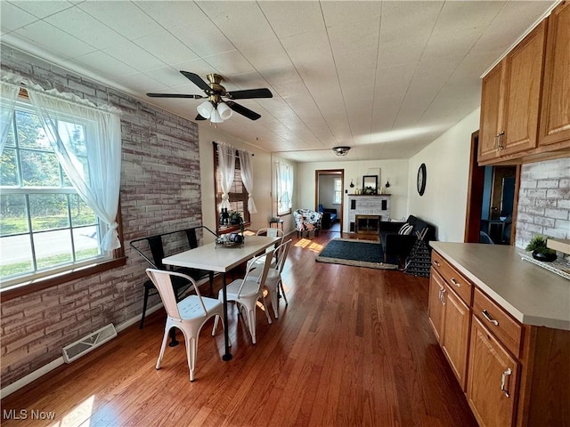 dining area with ceiling fan, dark hardwood / wood-style flooring, brick wall, and a brick fireplace