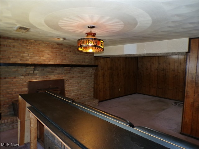 recreation room with wood walls, carpet flooring, and brick wall