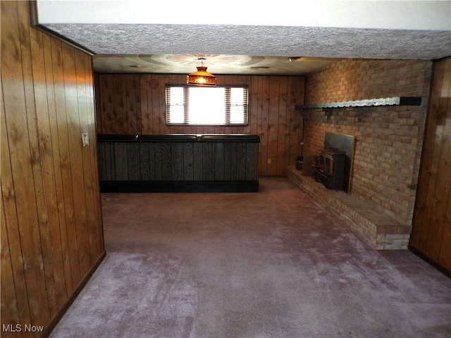 unfurnished living room with wood walls, a wood stove, dark carpet, and a textured ceiling