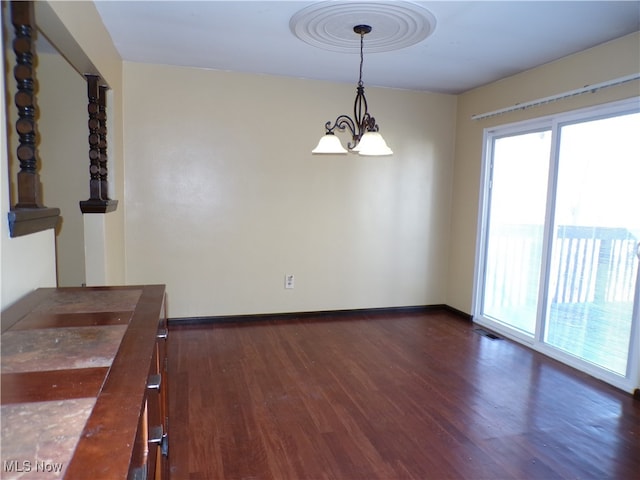 empty room with dark wood-type flooring and an inviting chandelier