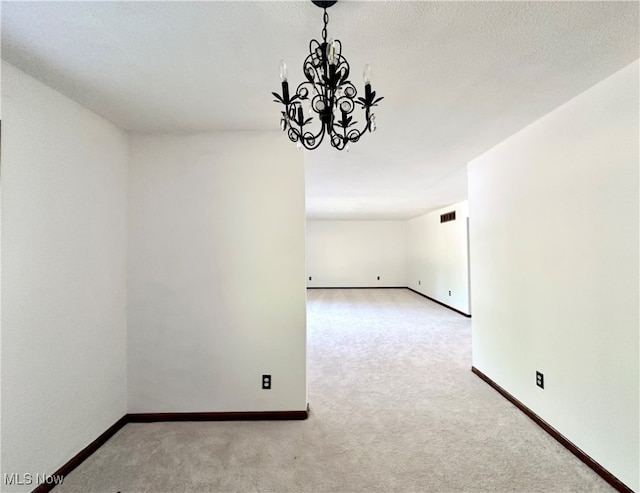 unfurnished room featuring a textured ceiling, light colored carpet, and a notable chandelier