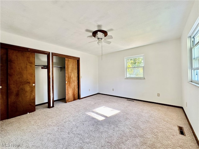 unfurnished bedroom featuring light carpet, multiple closets, ceiling fan, and a textured ceiling