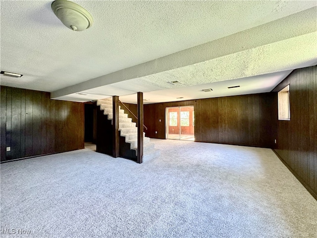 basement featuring carpet floors, a textured ceiling, and wooden walls