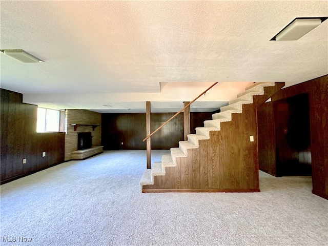 basement featuring a brick fireplace, wooden walls, a textured ceiling, and carpet floors