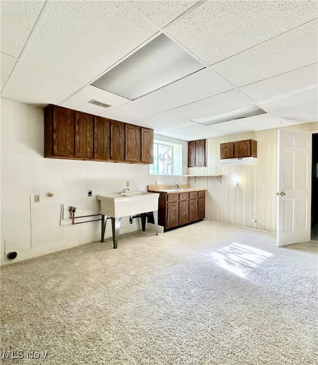 kitchen with a drop ceiling, wooden walls, sink, and light colored carpet